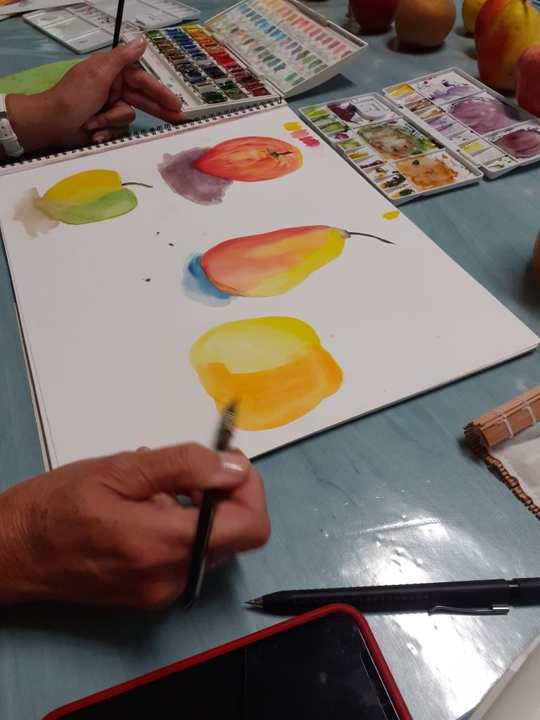 Personne entrain de peindre à l'aquarelle des fruits tel que des pommes et des poires