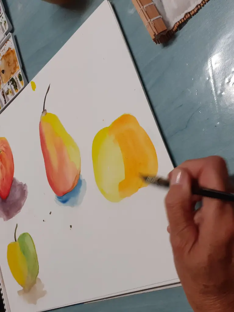 Personne entrain de peindre à l'aquarelle des fruits tel que des pommes et des poires